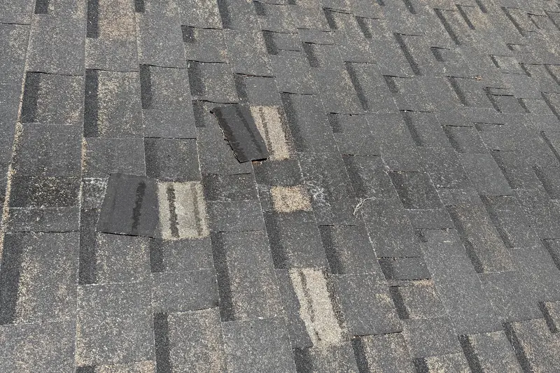 Cracked and torn shingles in the middle of a gray shingle roof