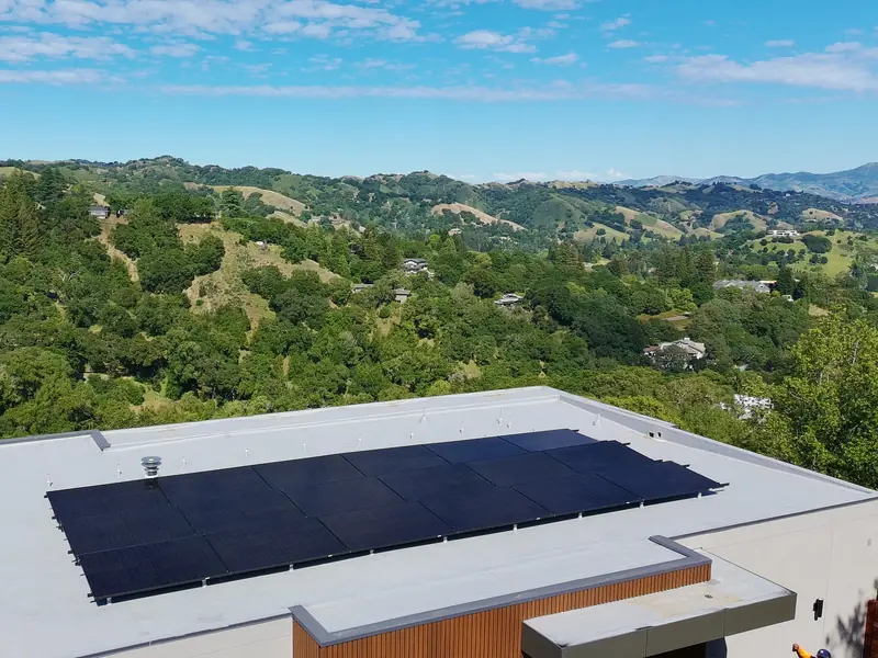 Black solar panels installed by GoSimpleSolar on a flat roof in Orinda, CA, with hills behind
